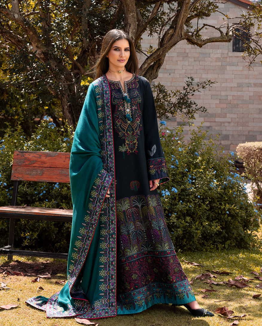Woman wearing a navy blue long embroidered winter suit with a teal embroidered shawl standing in a garden near a wooden bench