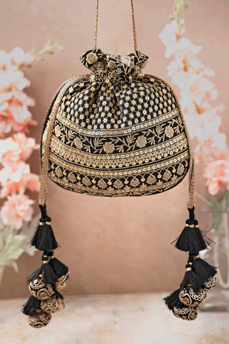 Black potli bag with intricate gold floral embroidery and sequin accents, drawstring closure with black tassels and decorative gold ornaments.