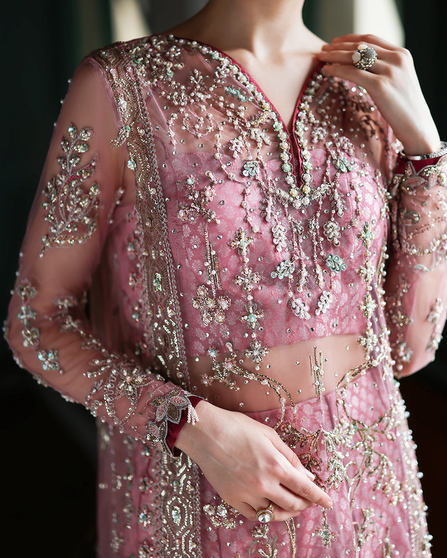 Woman posing in embroidered pink dress with hand-embellished sheer sleeves, wearing statement earrings and ring