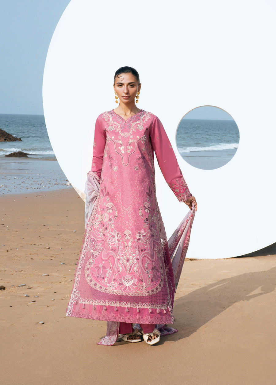 Woman wearing a pink embroidered lawn 3-piece suit standing on the beach with ocean background