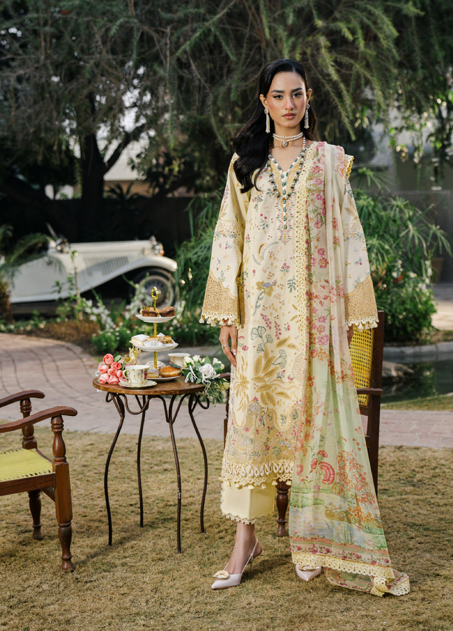 Model wearing embroidered luxury lawn suit in butter yellow standing beside garden table with tea set and flowers