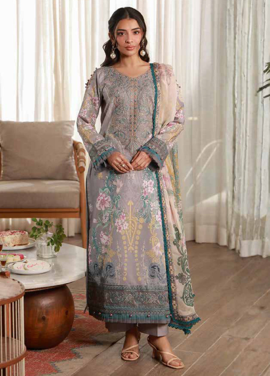 Front view of woman wearing elegant embroidered lawn suit in muted gray with floral embroidery and embroidered organza neckline standing in a cozy living room