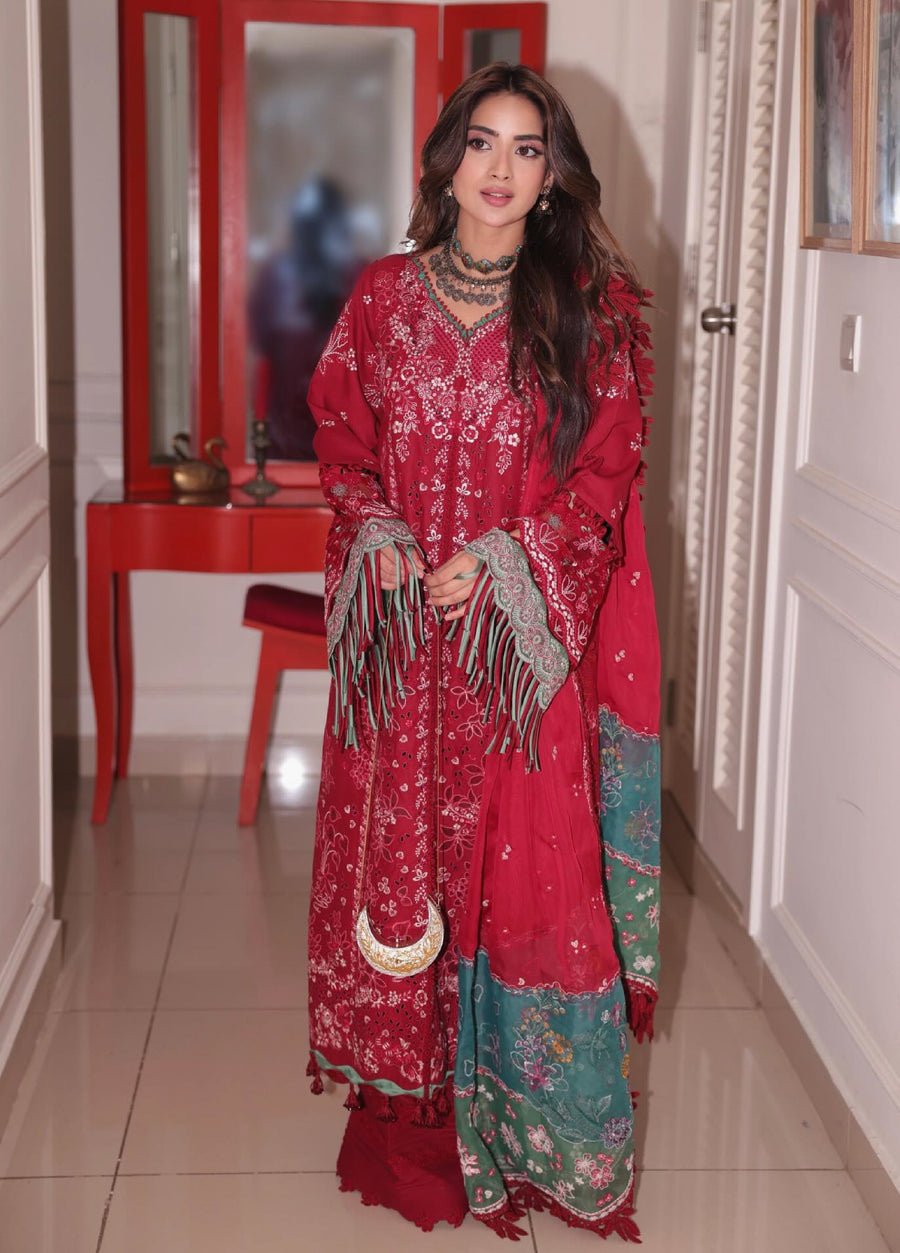 Woman modeling a red embroidered luxury lawn 3-piece suit with green lace and fringes in a hallway setting