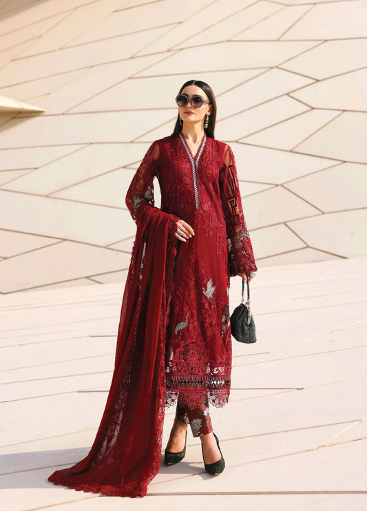 Woman wearing a deep red embroidered lawn suit with sheer sleeves and detailed florals, carrying a black handbag.