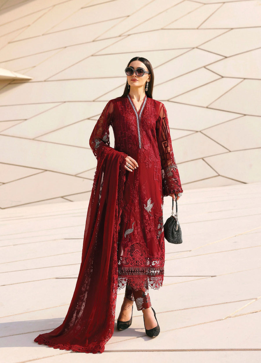Woman wearing a deep red embroidered lawn suit with sheer sleeves and detailed florals, carrying a black handbag.