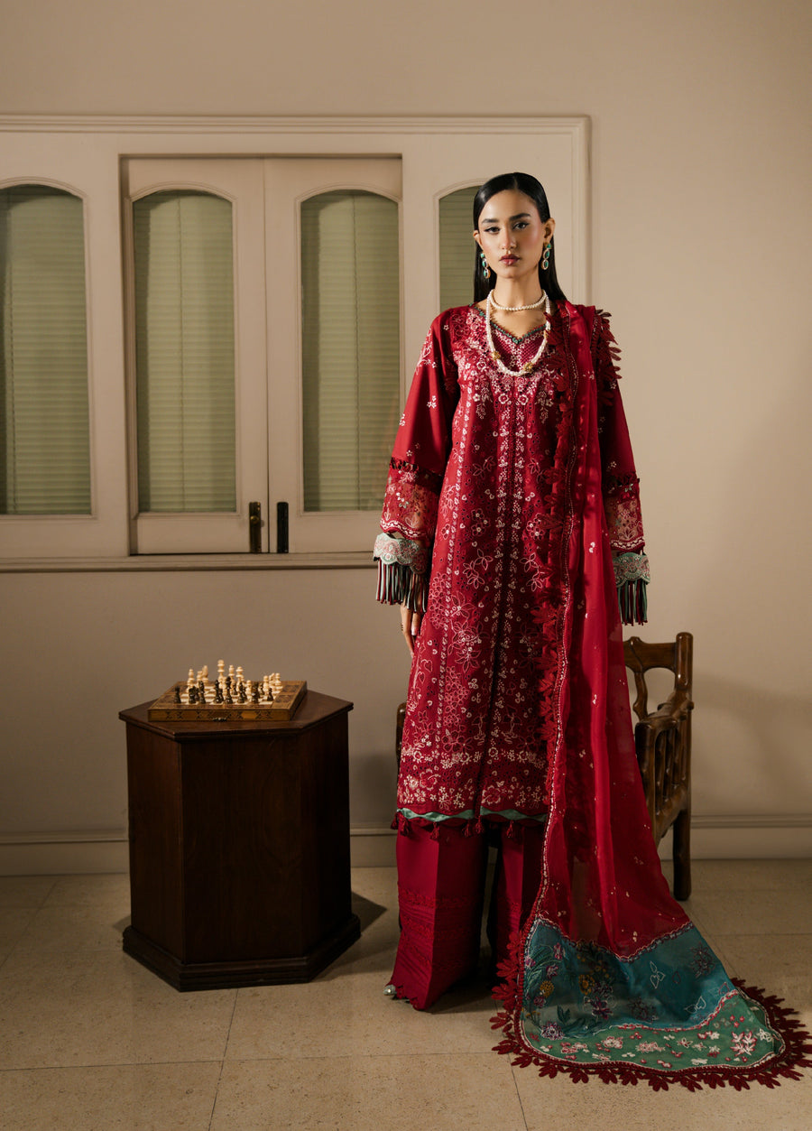 Fashion-forward model posing in red embroidered suit with matching dupatta draped elegantly over one shoulder inside a room