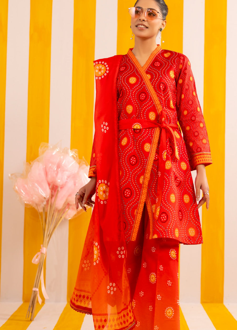 Front view of woman wearing vibrant red printed lawn suit with wrap shirt, wide trousers, and matching dupatta, posing against yellow and white striped background