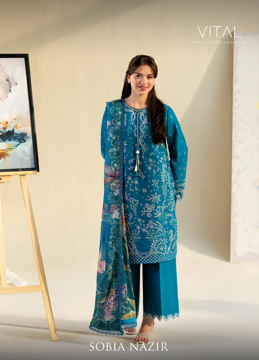 Woman modeling teal embroidered lawn 3-piece suit with floral details and printed chiffon dupatta, standing near an easel with artwork