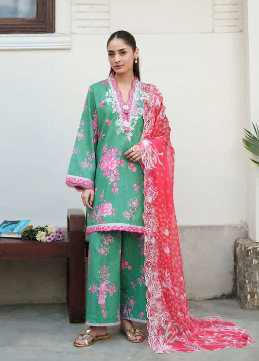 Woman wearing a green embroidered floral lawn suit with pink floral prints and a pink embroidered chiffon dupatta, standing near a wooden bench.