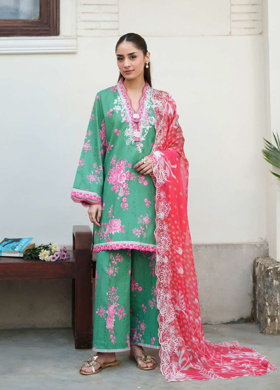 Woman wearing a green embroidered floral lawn suit with pink floral prints and a pink embroidered chiffon dupatta, standing near a wooden bench.