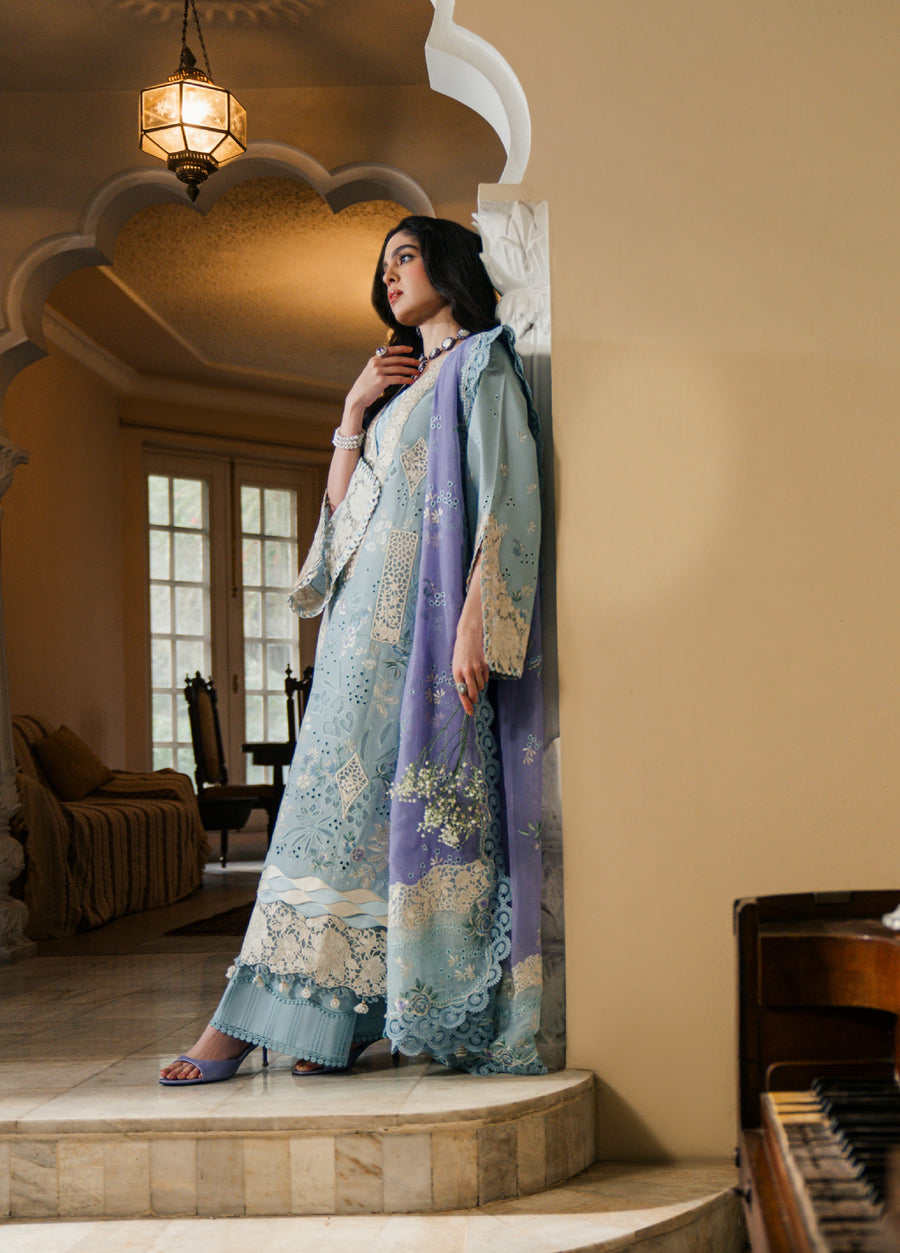Woman in elegant embroidered ice blue luxury lawn three-piece suit standing by arched doorway indoors