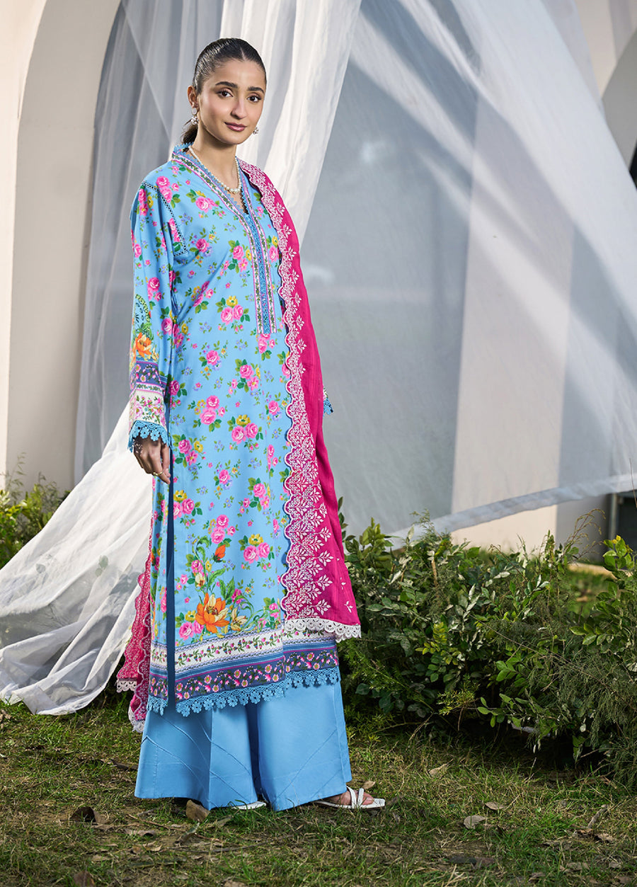 Woman wearing sky-blue floral printed long lawn shirt with blue lace trim, bright fuchsia embroidered dupatta, and solid blue cambric wide trousers standing outdoors