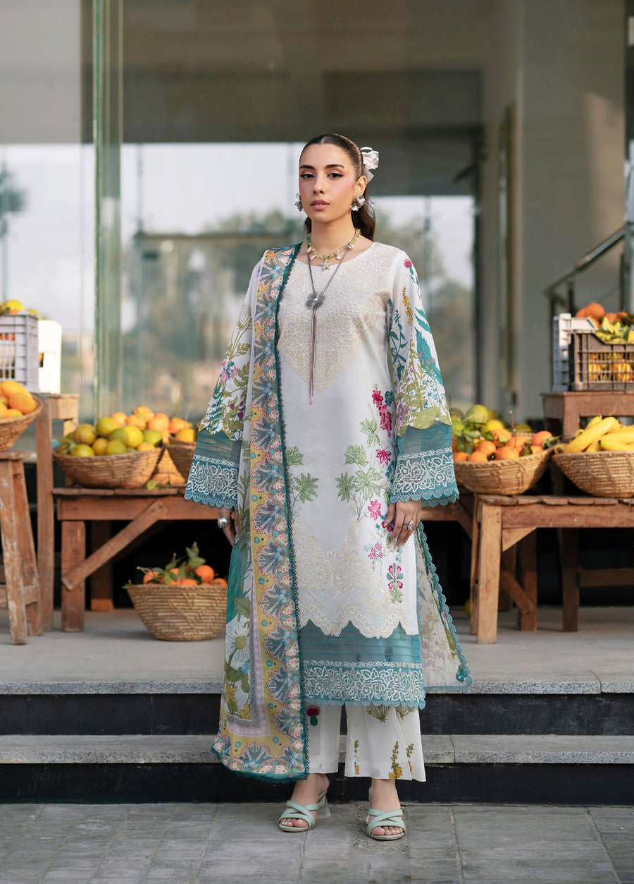 Front view of woman wearing elegant white and teal embroidered lawn 3-piece suit with floral patterns and lace-trimmed sleeves, standing outdoors with fruit baskets in the background.