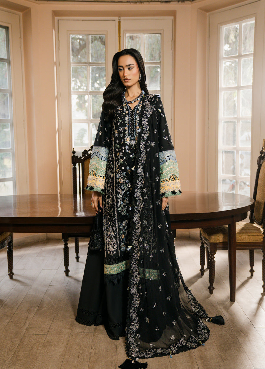 Woman wearing an elegant black embroidered 3-piece suit standing by a wooden table in a room with large windows