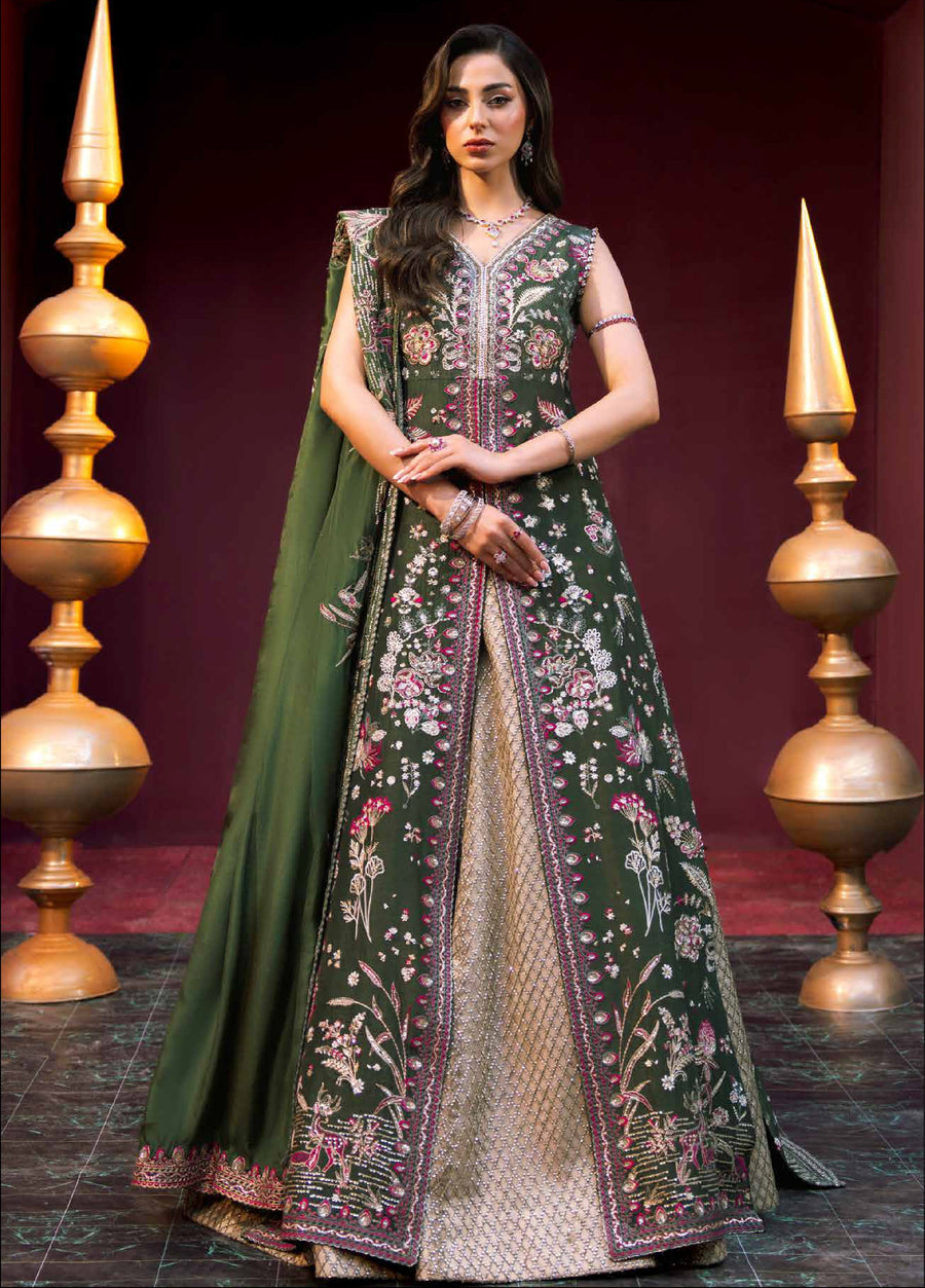 Front view of a woman wearing a dark green sleeveless embroidered long tunic with floral motifs over a golden lehenga skirt, accessorized with matching jewelry, standing between decorative golden pillars.