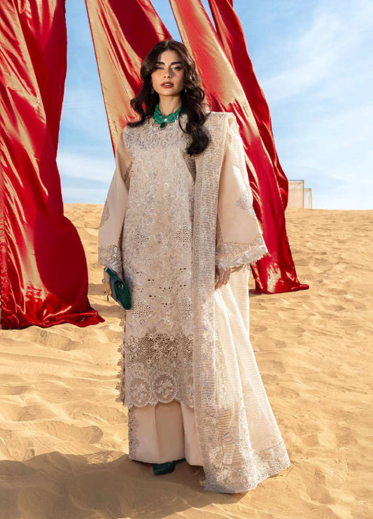 Woman standing on sand dunes wearing beige embroidered formal lawn suit with intricate floral embroidery and a matching dupatta under sunny sky