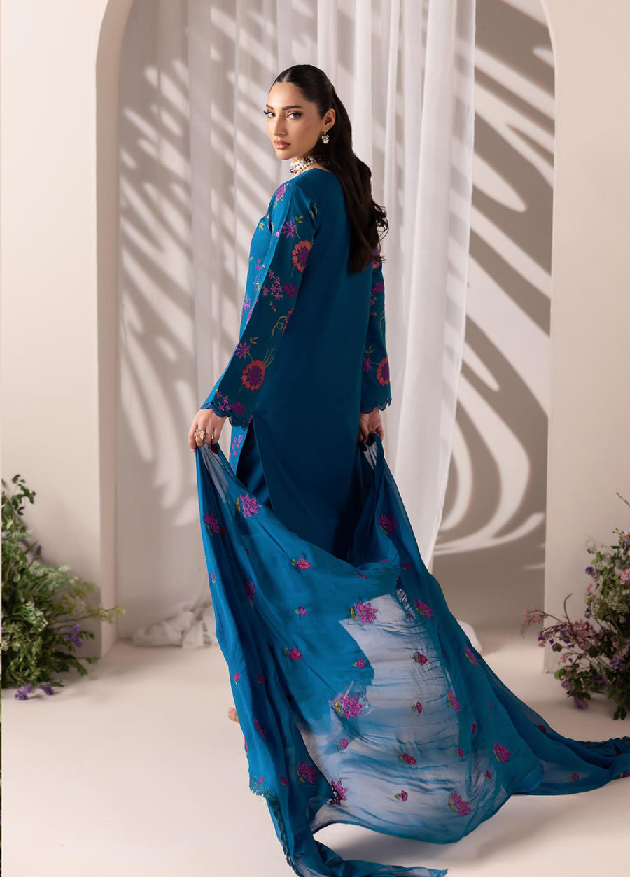 Back view of a woman dressed in a blue embroidered lawn suit holding the flowing chiffon dupatta, showcasing embroidered motifs and scalloped edges