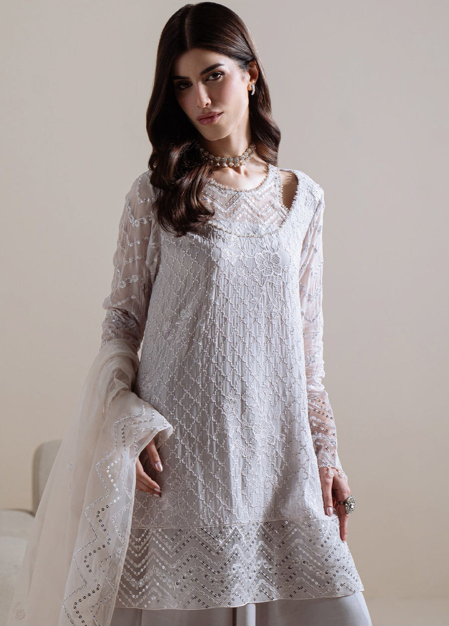 Close-up of upper torso showing intricate white embroidery on chiffon tunic with sheer sleeves and sequin accents, styled with pearl choker necklace