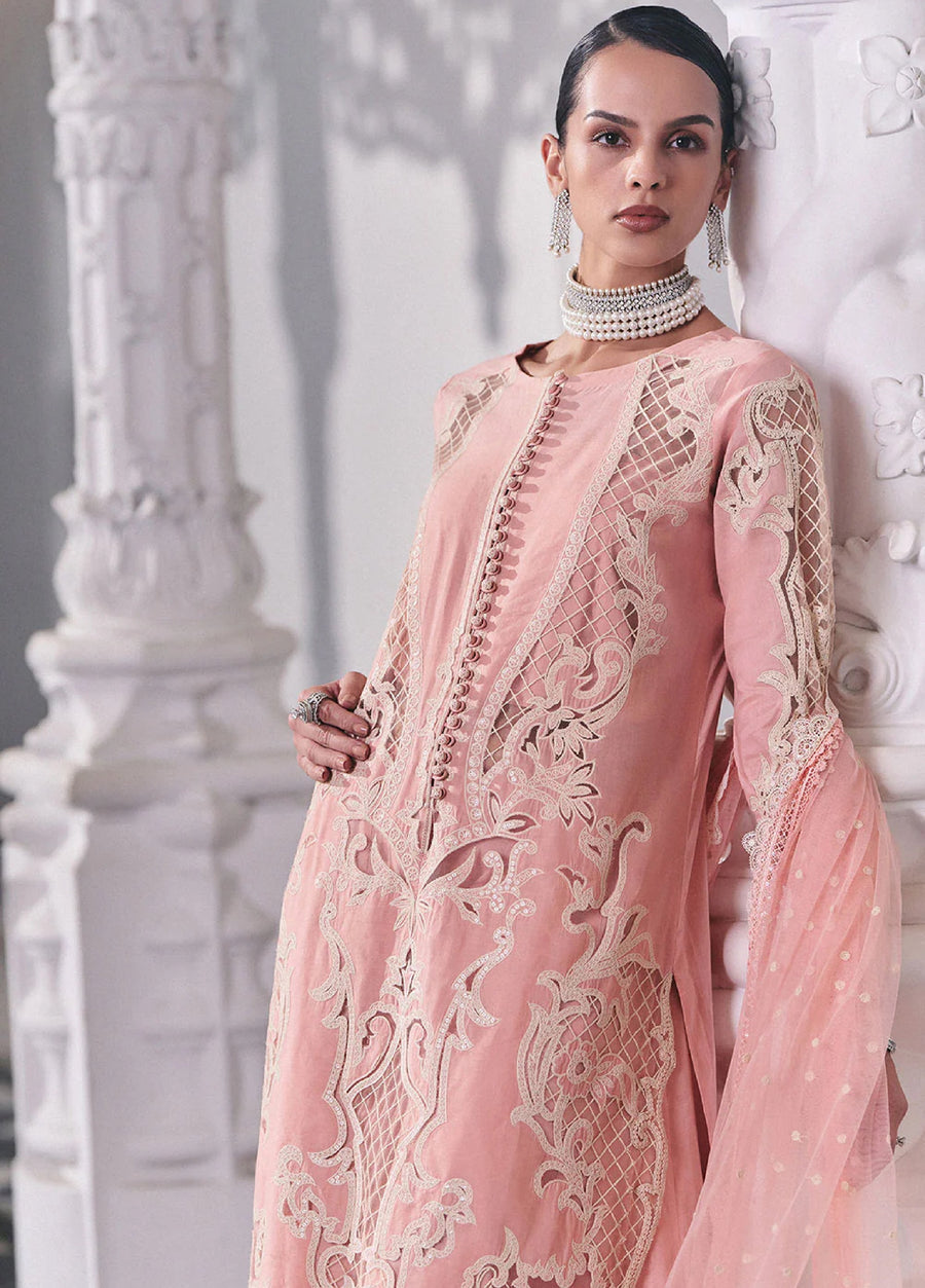 Close-up of model showcasing detailed embroidery and fabric-covered buttons on the front of the pink lawn suit, paired with pearl jewelry.