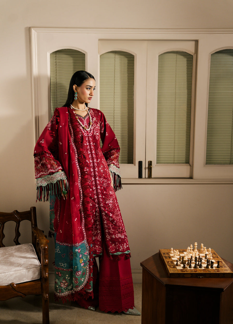 Side profile of woman showcasing detailed embroidery on sleeve and neckline of red 3-piece ethnic suit with pearl necklace