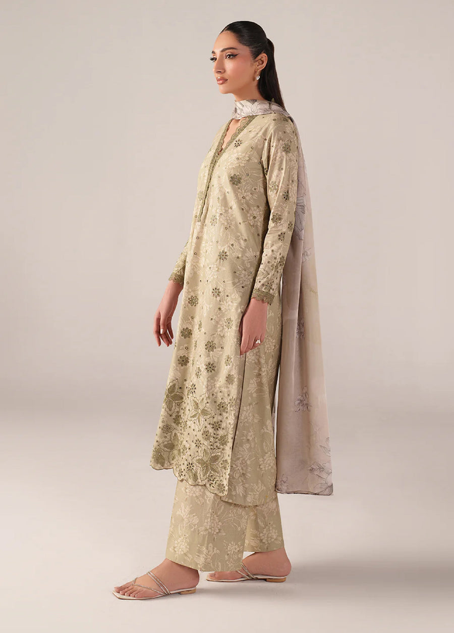 Side profile of woman modeling beige embroidered lawn suit with detailed floral embroidery on sleeves and front, showing chiffon dupatta draped over shoulder