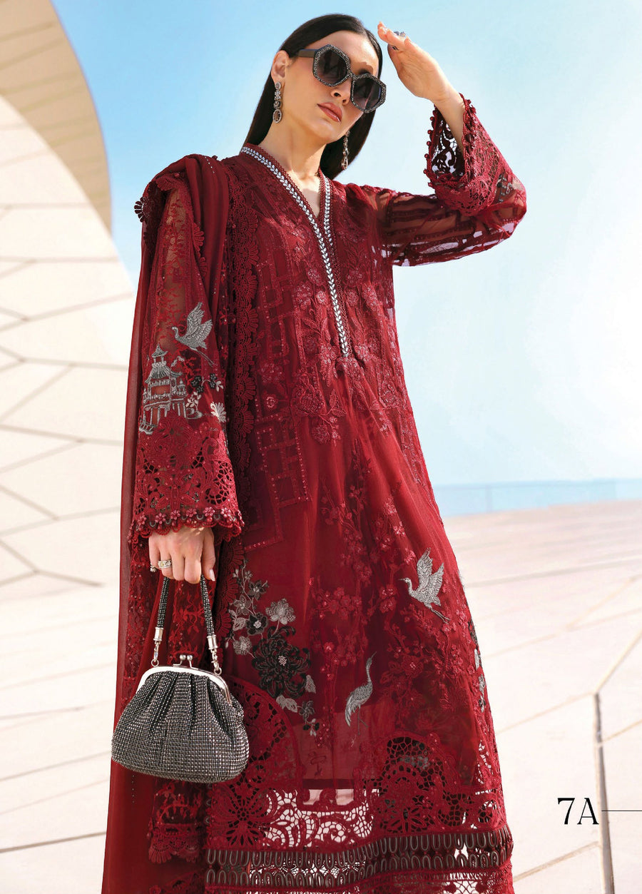 Close-up of a woman in a red embroidered lawn suit showcasing intricate sleeve embroidery and lace borders, accessorized with a black handbag and statement earrings.