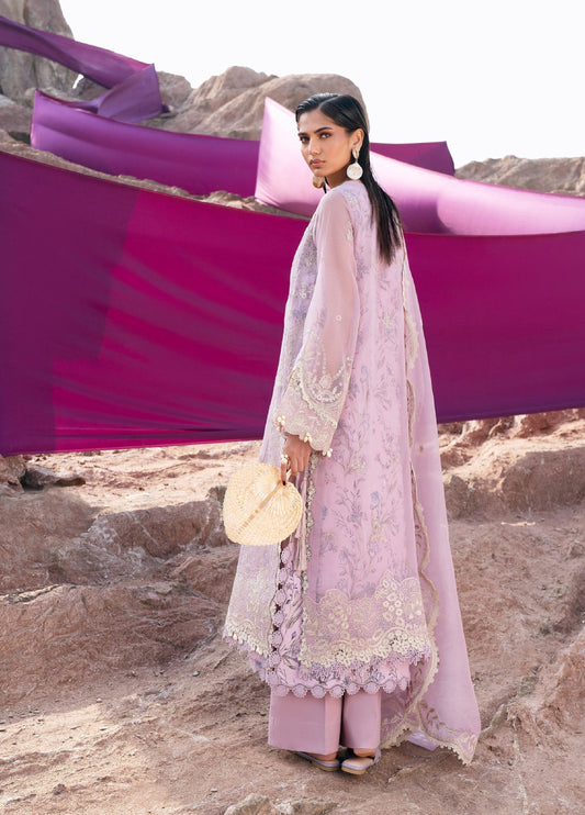 Rear view of a woman in a lilac embroidered 3-piece suit showing detailed floral embroidery on the back, lace cuffs, wide-leg trousers, and a draped matching dupatta with purple fabric backdrop.