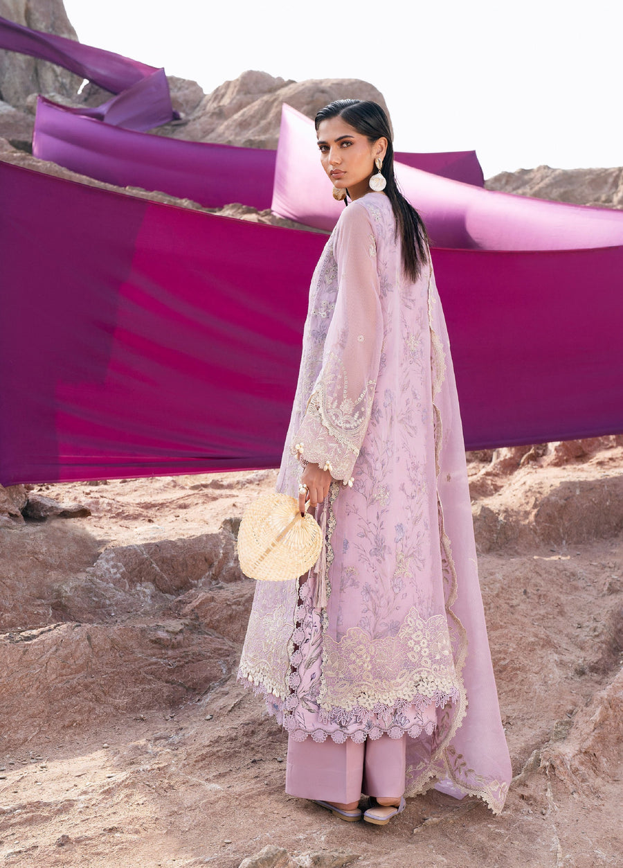 Rear view of a woman in a lilac embroidered 3-piece suit showing detailed floral embroidery on the back, lace cuffs, wide-leg trousers, and a draped matching dupatta with purple fabric backdrop.