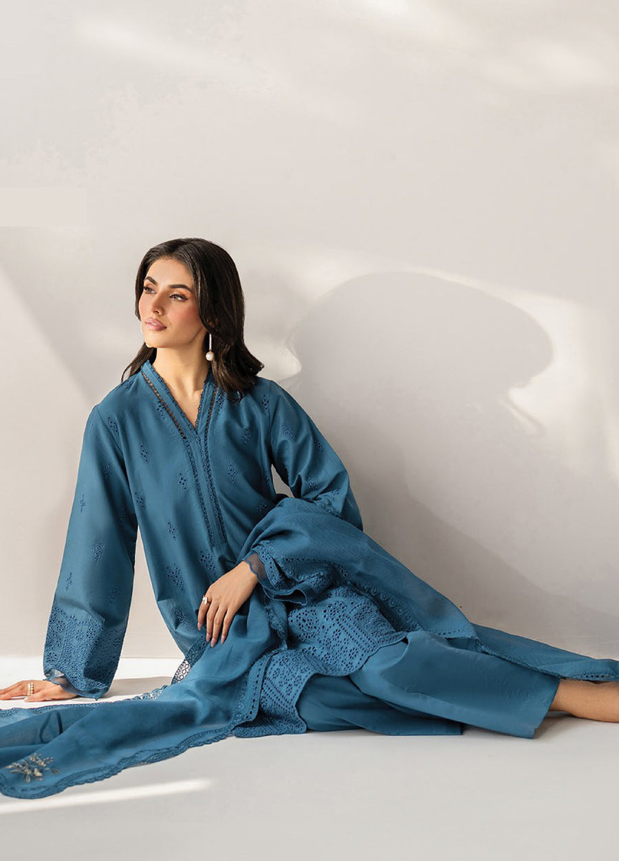 Woman sitting gracefully wearing a teal blue embroidered lawn suit with intricate cutwork embroidery and a matching embroidered dupatta, styled for modest formal wear