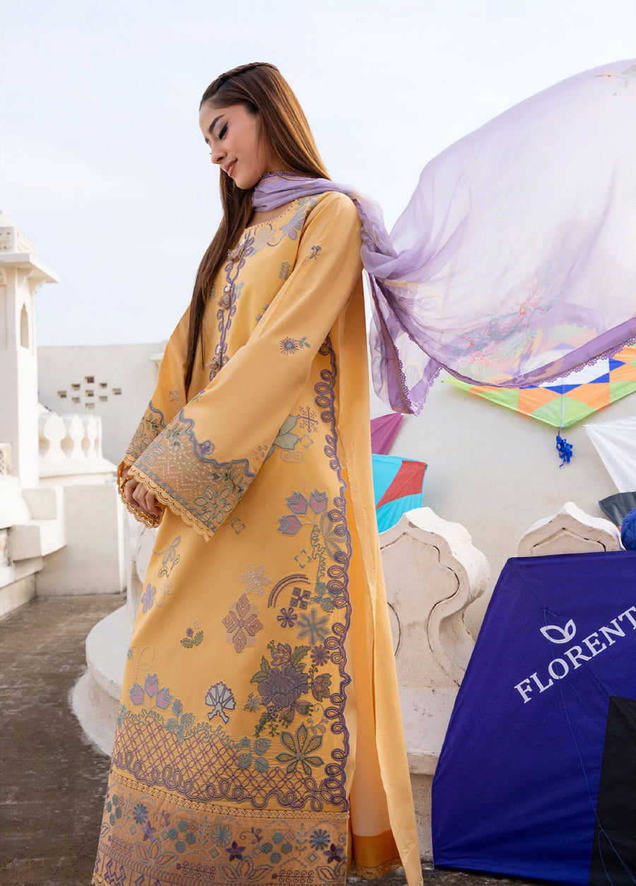 Close-up of woman in mustard yellow embroidered lawn shirt showing intricate embroidery on sleeves and hem with lavender chiffon dupatta draped behind, outdoor setting with white walls and kites