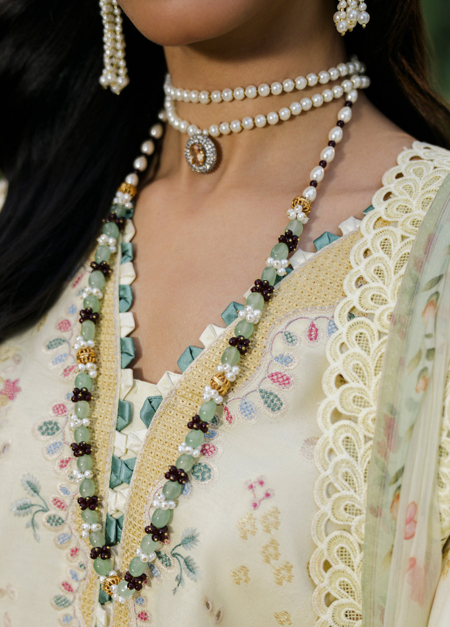 Close-up of earrings, pearl choker necklace, and green gemstone necklace worn with embroidered yellow lawn suit
