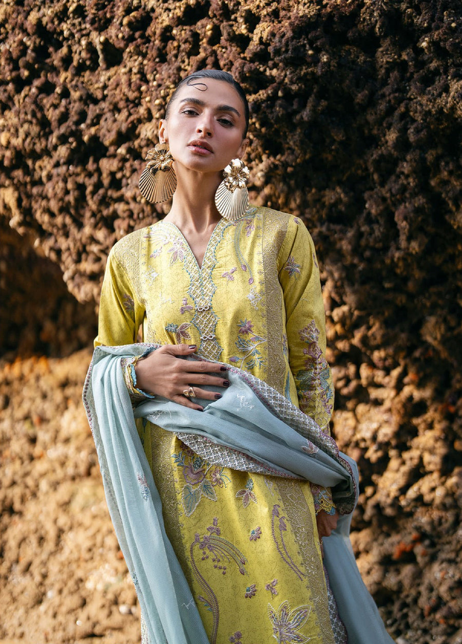 Close-up of woman wearing the yellow embroidered lawn suit with intricate neckline and sleeve embroidery, holding the light blue embroidered dupatta in front of a rocky background.