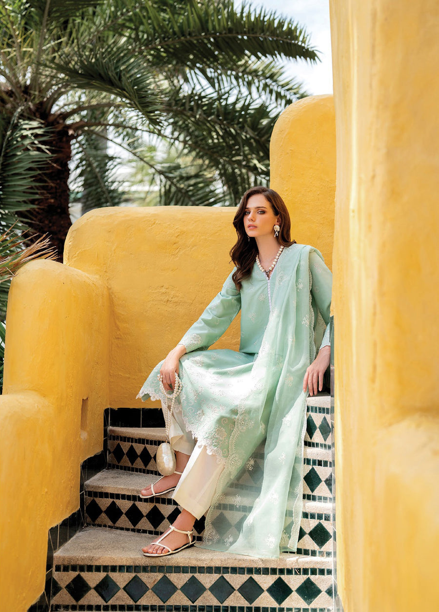 Woman seated on patterned steps in pastel green embroidered lawn suit with matching dupatta, accessorized with pearl earrings and sandals