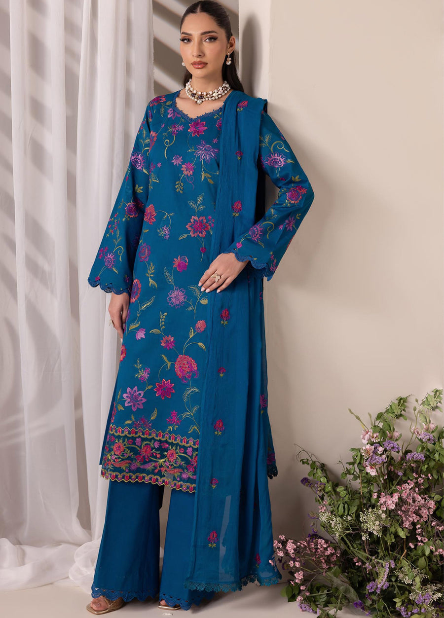 Front side view of a woman posing in a blue floral embroidered lawn suit set with scalloped hem details on sleeves and trousers, holding the dupatta