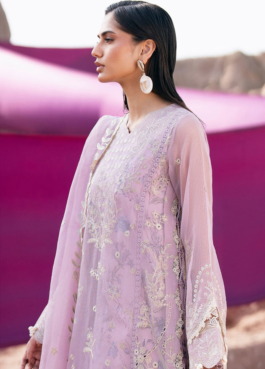 Close-up of woman in lilac embroidered suit highlighting sheer sleeves with lace and pearl tassels and detailed floral embroidery on the front, paired with statement shell drop earrings.