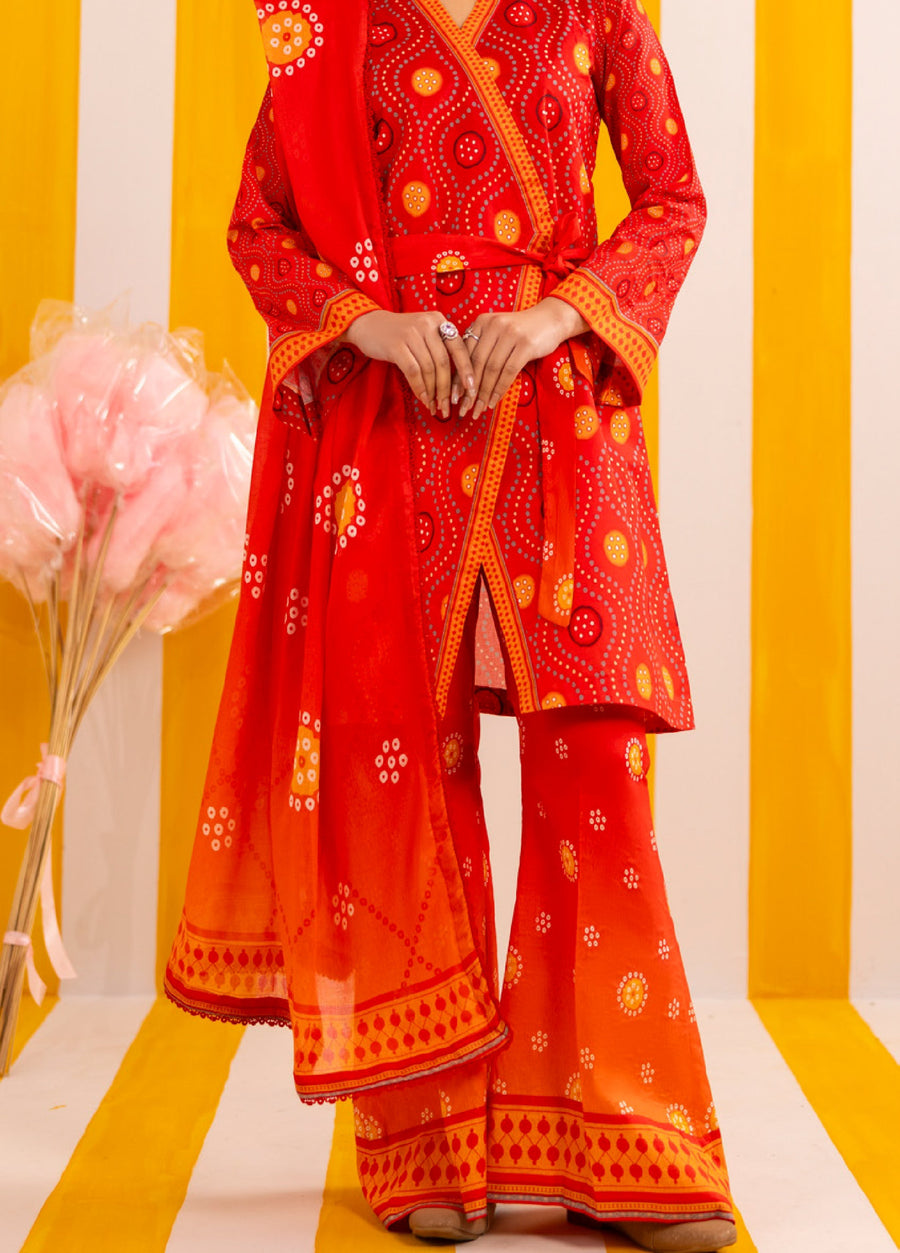 Side front view of woman wearing bright red printed lawn suit with coordinated wide-legged trousers and border printed dupatta, standing on striped floor