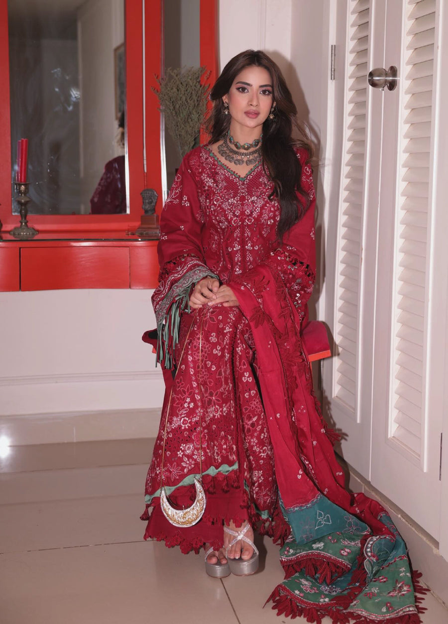 Full-length view of woman standing in red embroidered 3-piece suit featuring floral patterns and fringed borders beside a wooden side table