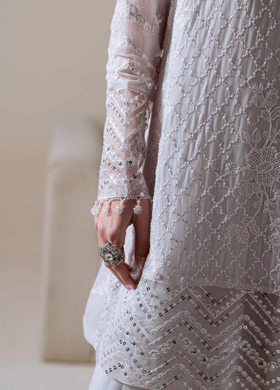 Close-up of hand and lower sleeve showing delicate bead and sequin embroidery on sheer fabric with zigzag accents near the hem of the tunic