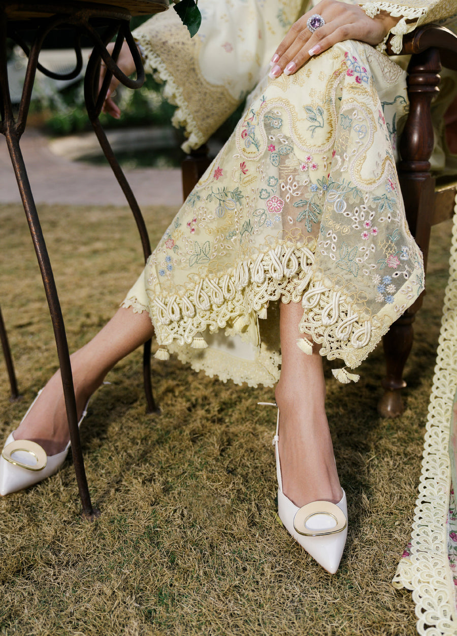 Detailed view of embroidered floral pattern and lace hemline on the model’s lawn suit paired with pointed toe heels