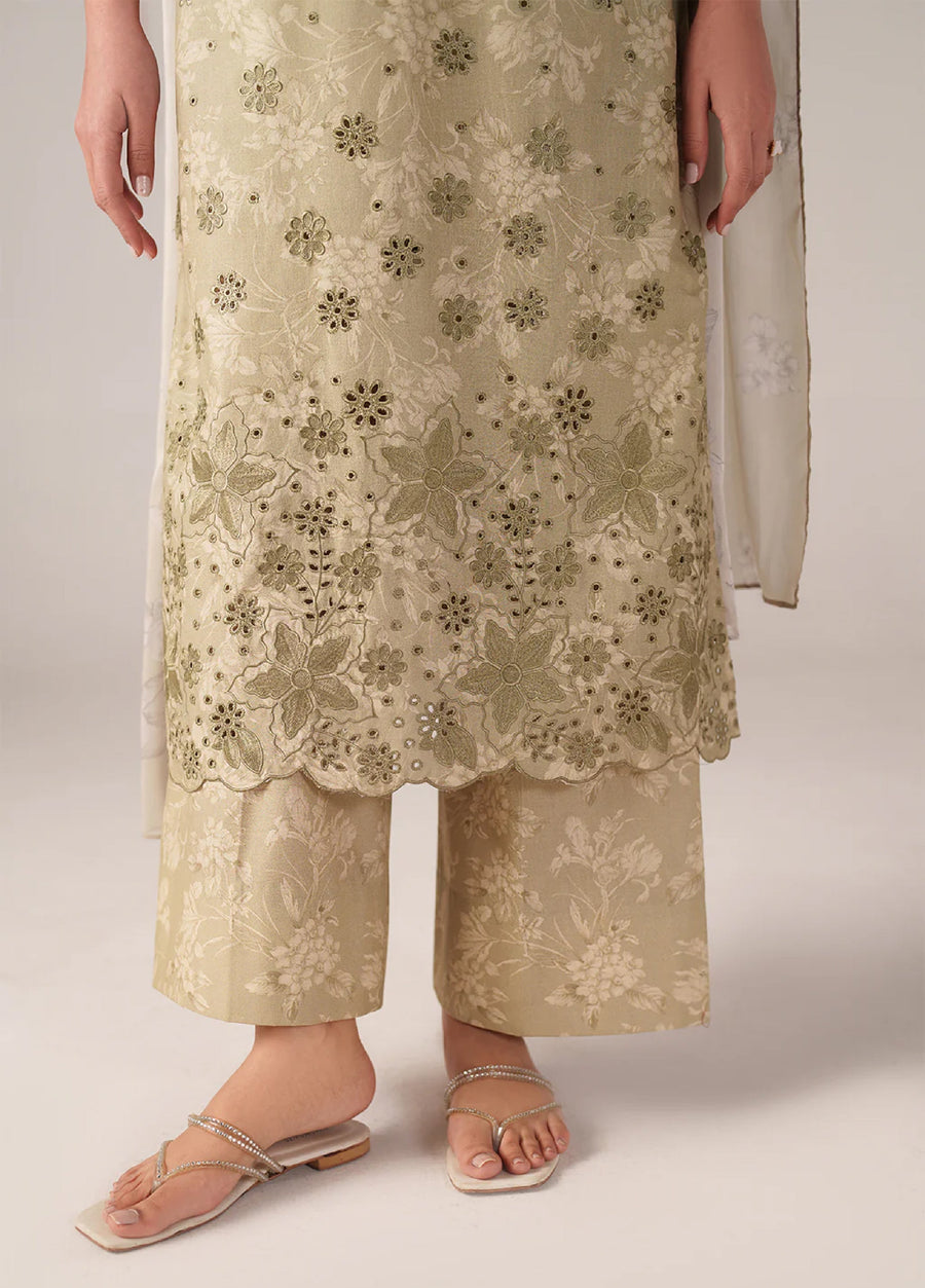Close-up detail of bottom hem of embroidered shirt with scalloped edge and floral embroidery above wide-legged printed trousers