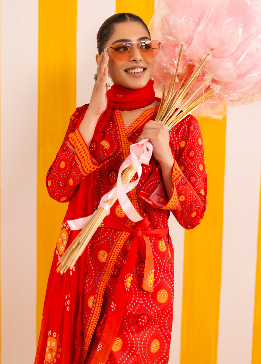 Woman smiling and holding a bouquet of pink cotton candy sticks, dressed in red printed lawn suit with wrap shirt and coordinating dupatta