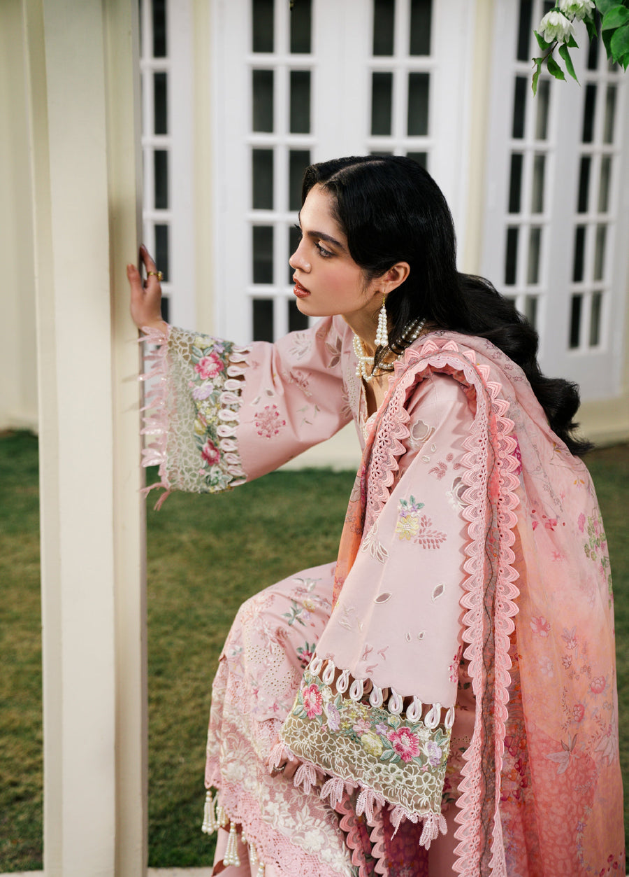 Side view of woman in baby pink embroidered suit crouching near a tree with floral embroidery and lace details on the sleeves.