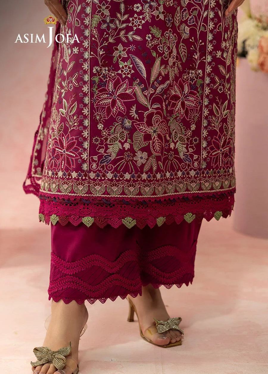 Close-up of feet wearing golden heeled sandals with bow detail paired with magenta embroidered pants scalloped at the hem.