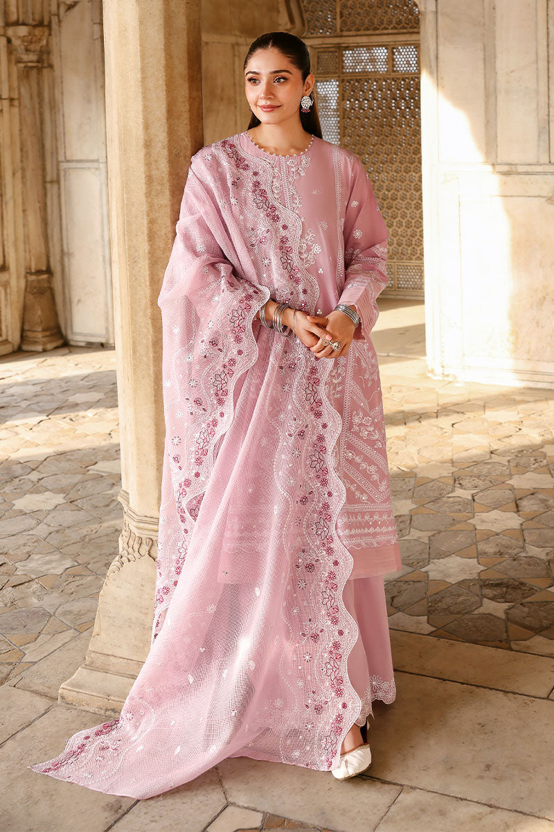 Woman wearing a pastel pink embroidered lawn suit with net dupatta standing by a carved pillar