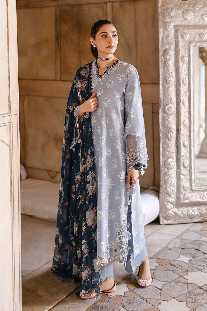 Woman wearing sky blue embroidered lawn suit holding navy floral printed chiffon dupatta standing indoors