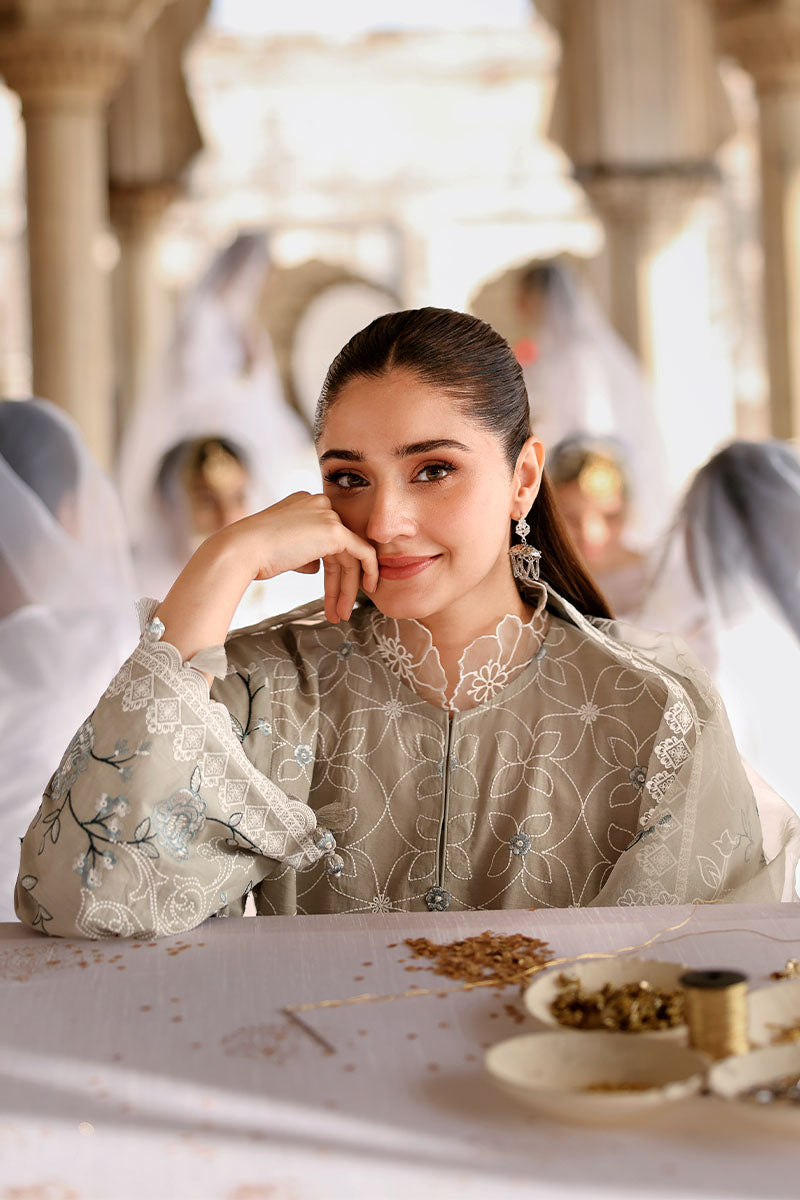 Portrait of woman in beige embroidered lawn suit with delicate floral embroidery, smiling and resting her chin on her hand in an indoor setting