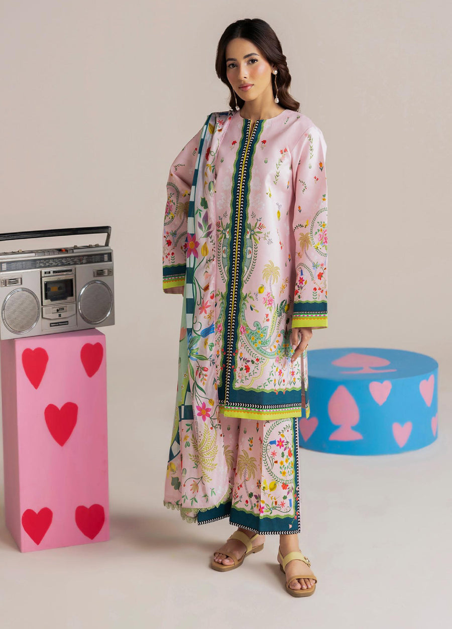 Woman modeling elegant pastel pink floral printed lawn suit with long shirt, matching trousers, and dupatta standing next to retro radio and colorful props
