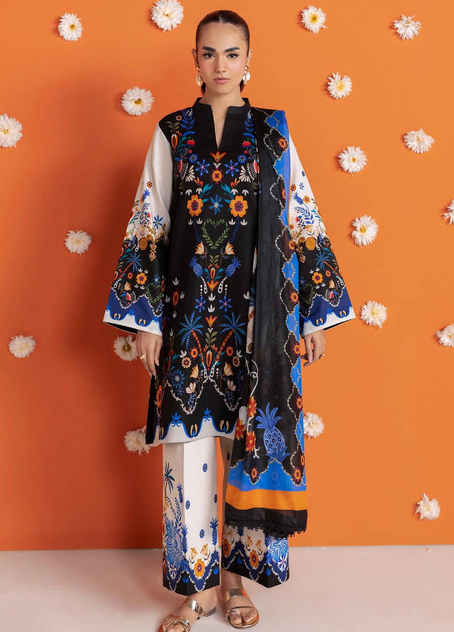 Woman standing wearing a black floral printed lawn suit with cream and blue wide-leg trousers and matching dupatta against an orange floral background
