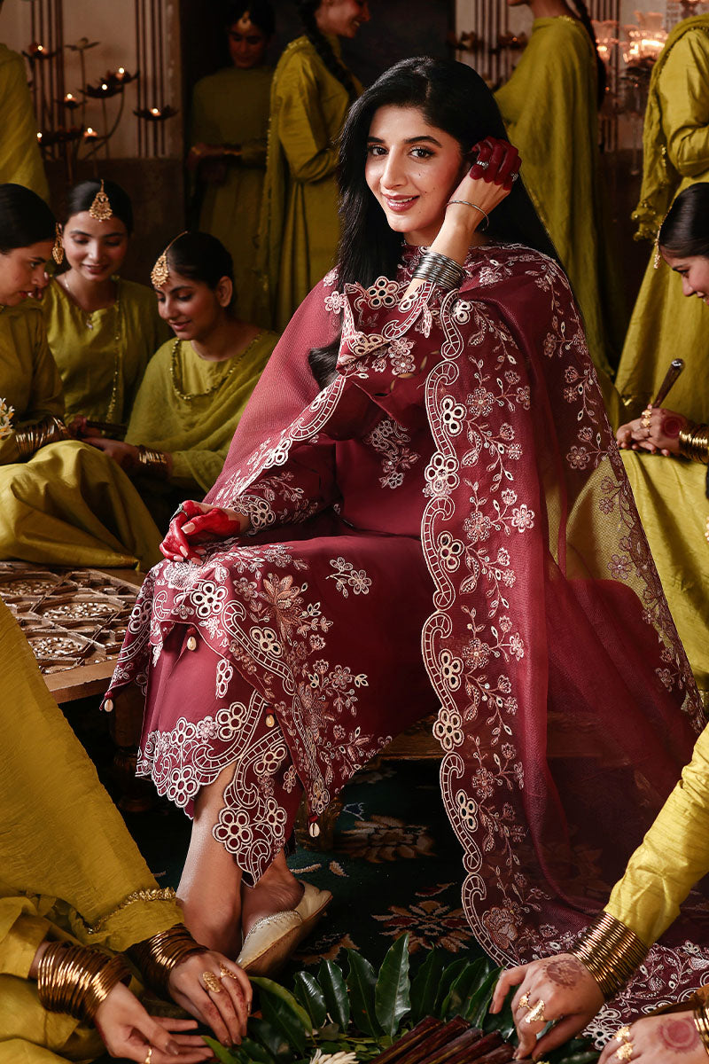 Woman seated wearing an embroidered crimson lawn suit with detailed floral embroidery and matching dupatta, surrounded by women in green dresses