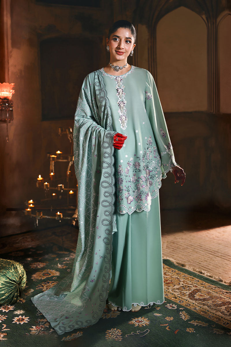 Woman wearing a pastel green embroidered lawn suit with floral decorations, standing gracefully with matching dupatta draped over her shoulder.